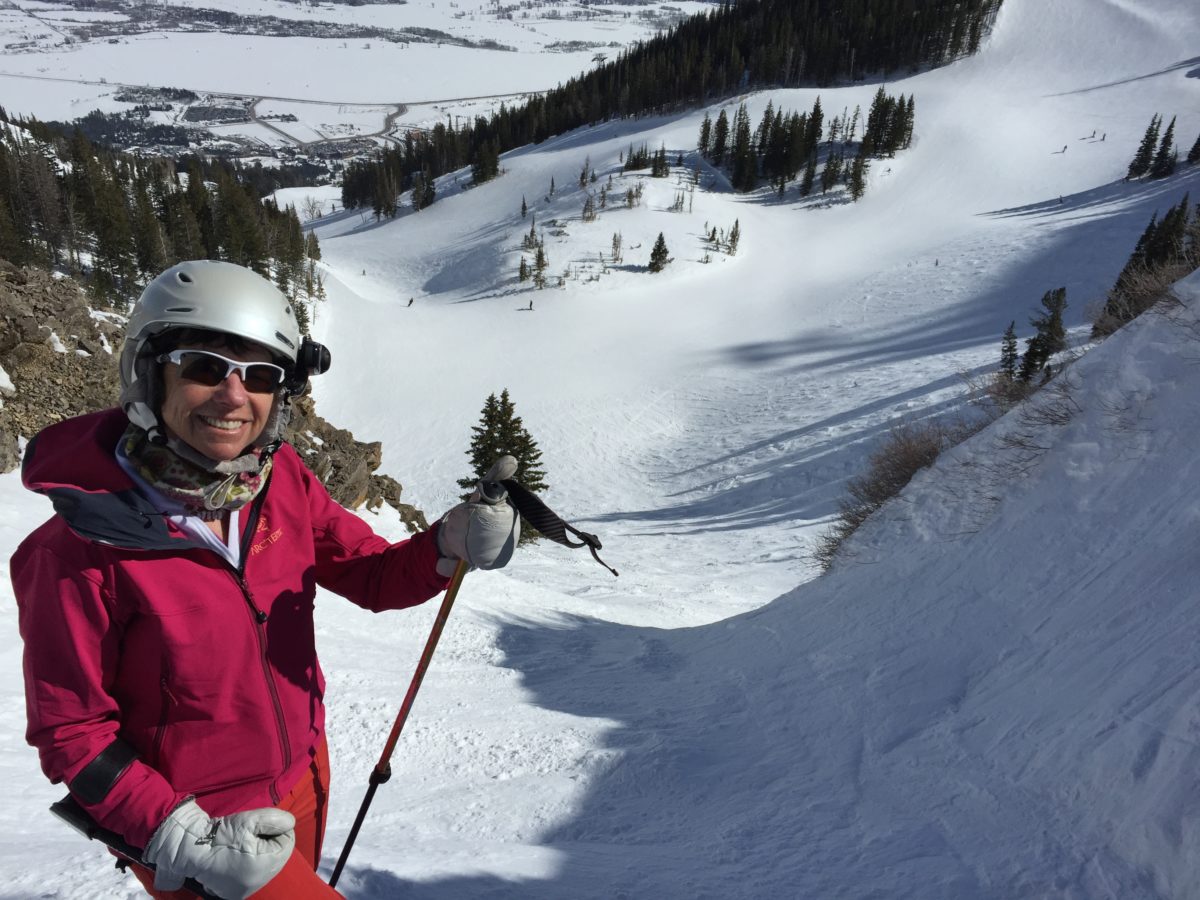 Janet in a pink ski jacket at the top of a steep snowy run, smiling